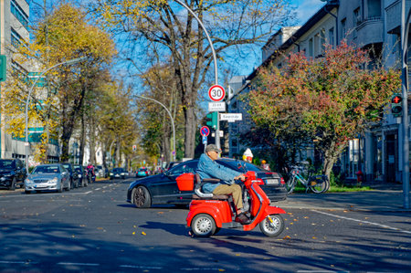 Berlin, Germany - November 04, 2023: Autumnal street scene in Berlin with crossing electric wheelchair.のeditorial素材