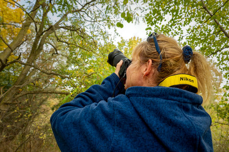 Berlin, Germany - October 25, 2021: Shot of a photographer in autumn from diagonally behind, focusing on an object with her camera.のeditorial素材