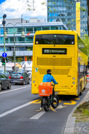 Berlin, Germany - April 27, 2024: Bicycle courier for food behind a public transport bus in the center of Berlin.のeditorial素材