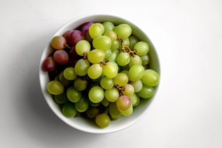 Green and purple grapes in a white bowl on a white background.の素材