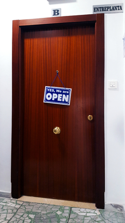 Brown flat door with a sign saying Yes We Are Open. Spanish building.の写真素材