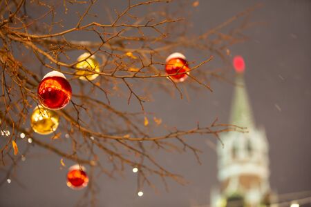 Trees, decorated with Christmas balls against the sky and buildings in the festive illumination. Snowfallの写真素材