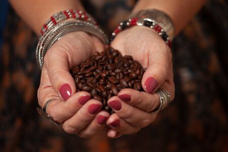 Women's hands in oriental jewelry hold a handful of coffee beansの写真素材