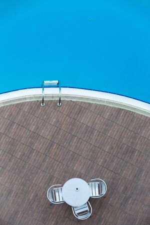 Top view on metal cafe table and three chairs near swimming pool  with blue water.の写真素材
