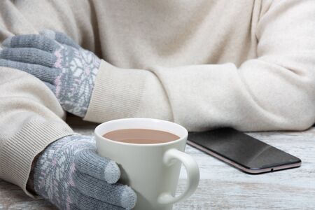 A man in warm clothes sits with a cup of hot drink in a street cafe.  Close-up. Rest during winter...