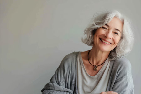 A portrait of a senior woman with silver hair and a timeless smile, exuding warmth and life satisfaction on a soft background.の素材