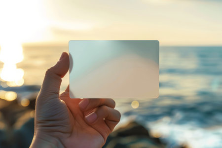 Hand presenting a plain card with a seascape backdropの素材
