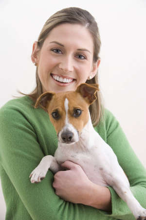A attractive young woman is wearing a green sweater and smiling while holding a dog. Vertical shot.の写真素材