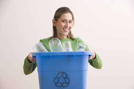 An attractive young woman his smiling and holding a blue recycle bin with plastic bottles in it. Horizontal shot.の写真素材