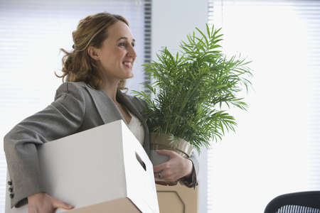 A young businesswoman smiles as she carries her office belongings in her hands.  Horizontal shot.の写真素材