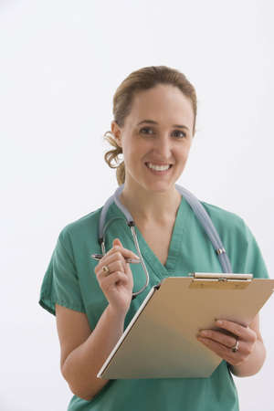 A young nurse is holding a clipboard while smiling at the camera. Vertical shot. Isolated on white.の写真素材