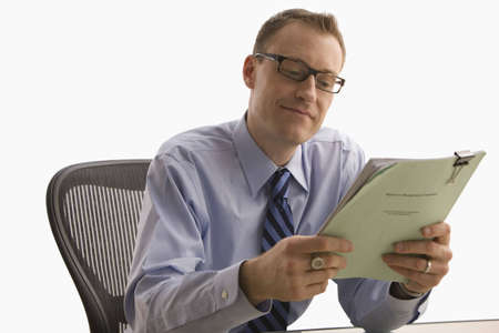 A businessman is seated at a desk and is looking at paperwork with a happy expression on his face.  Horizontal shot.  Isolated on white.の写真素材
