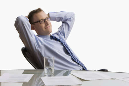 A businessman reclines back in his chair at work with paperwork spread across his table.  Horizontal shot.  Isolated on white.の写真素材