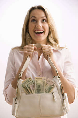 A young woman is holding a cash filled purse with large smile on her face.  Vertical shot.の写真素材