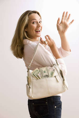 A young woman is holding a cash filled purse and waves back over her shoulder.  Vertical shot.の写真素材