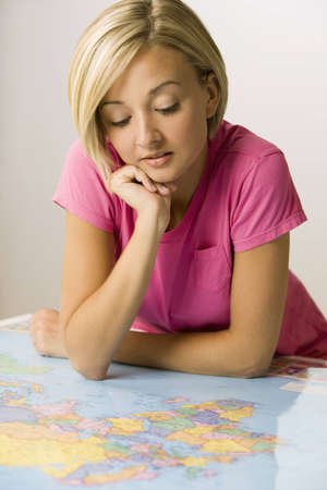 A young woman is leaning over a map and studying it.  Vertical shot.