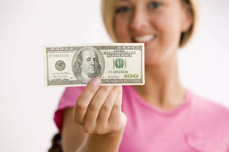 A young woman is holding out a $100.00 bill and smiling at the camera.  Horizontal shot.の写真素材