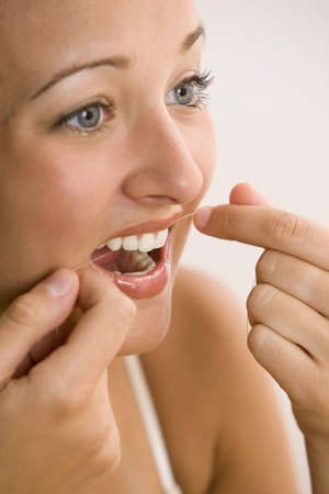A young woman is flossing her teeth while looking to the side.  Vertical shot.の写真素材