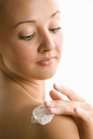 A young woman is rubbing lotion into her shoulder.  Vertical shot.の写真素材