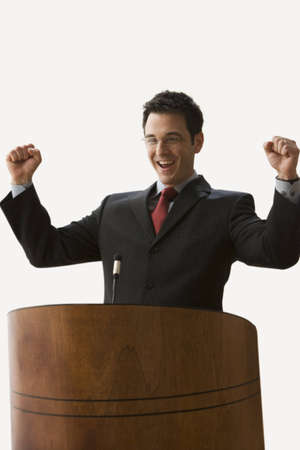 A young businessman is standing at a podium with fists raised. Vertical shot. Isolated on white.の写真素材