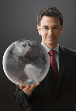 A handsome businessman is smiling at the camera while holding a clear globe. Vertical shot.の写真素材