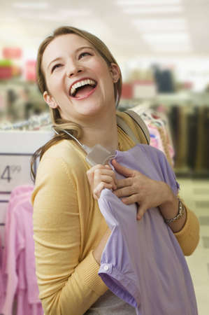 A beautiful young woman excitedly picks out a blouse while shopping.  Vertical shot.の写真素材