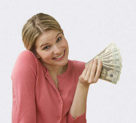 Beautiful young woman fans out cash and shrugs her shoulders.  Square shot.の写真素材