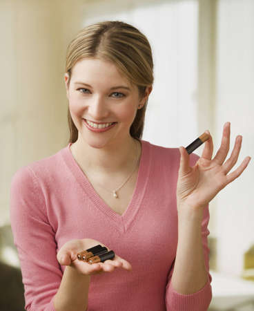 Attractive young woman holds up a set of AA batteries in her hands.  Vertical shot.の写真素材