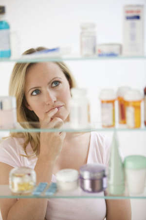 A young woman is looking through her medicine cabinet.  Vertical shot.の写真素材