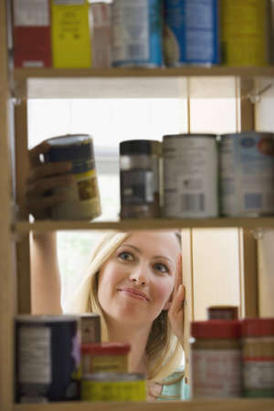A young woman is smiling as she looks through kitchen cupboards.  Vertical shot.の写真素材