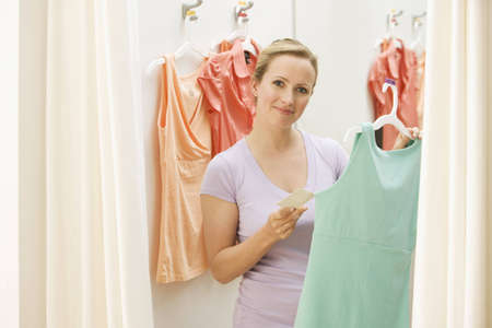 A young woman poses with clothing she has picked out in a store.  Horizontal shot.の写真素材