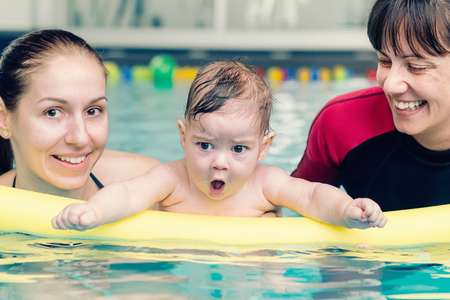 Swimming for babies - little baby boy in swimming pool with his mother and instructorの写真素材