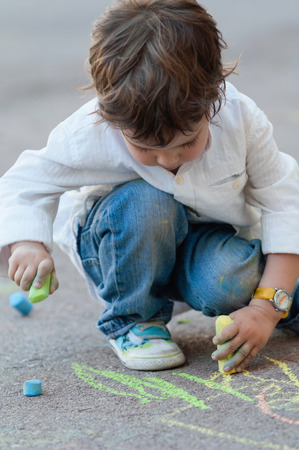 Little boy drawing with chalks on the streetの写真素材