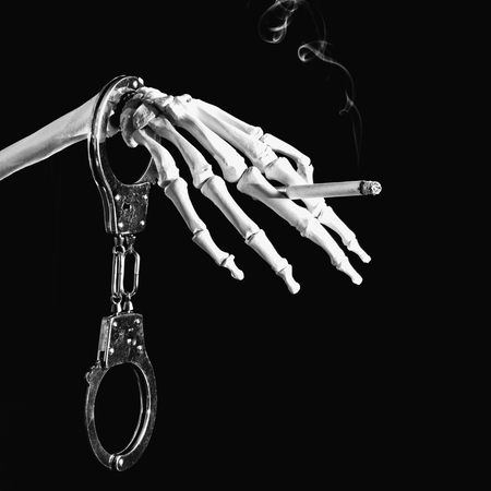 Smoking is addictive and deadly - clear and simple concept with handcuffs, skeleton and burning cigarette. Black and white image on black backgroundの写真素材
