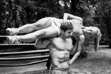 Cheerful fitness couple exercising in nature. Male athlete carrying woman on his shouldersの写真素材