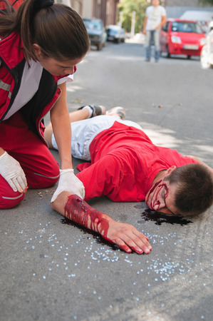 Paramedic with car accident victim on the street. Simulated exercise with doctor supervised realistic medical make-up.の写真素材