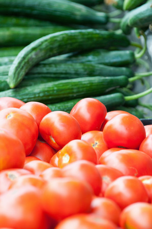 Fresh tomatoes and cucumbers on a market stall. Selective focus set on tomatoes in the centerの写真素材