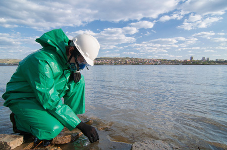 Technician in protective suit taking water samples from city reservoirの写真素材