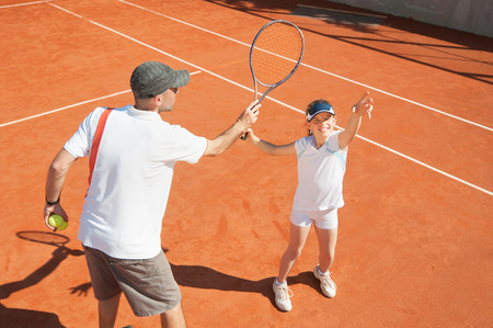 Young girl training with tennis instructor on clay courtの写真素材