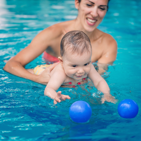 Cute baby boy swimming with his mother in the pool. Baby is trying to catch ballの写真素材