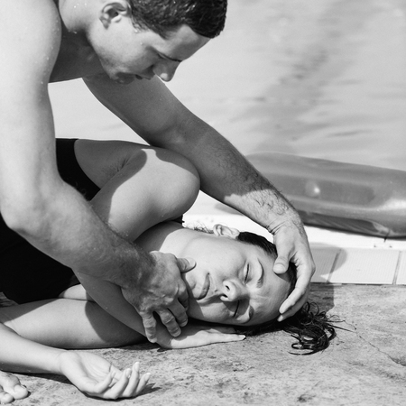 Lifeguard helping swimming pool accident victim. Positioning her on the side, opening airwaysの写真素材