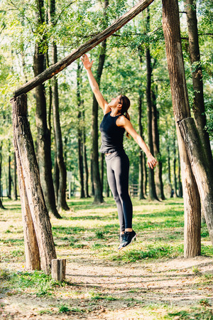 Young female athlete jumps to touch wooden beam on forest fitness trailの写真素材