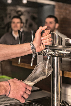 Bartender drawing beer in pub. Focus on hands, blurred people in backgroundの写真素材