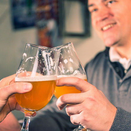 Friends toasting with wheat beer in pub. Focus on glasses, toned image.の写真素材