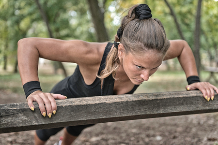 Female athlete doing push ups on wooden barrier