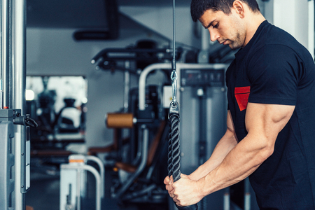 DSLR photo of muscular male athlete training on new exercising machine in modern gym. Model is body...