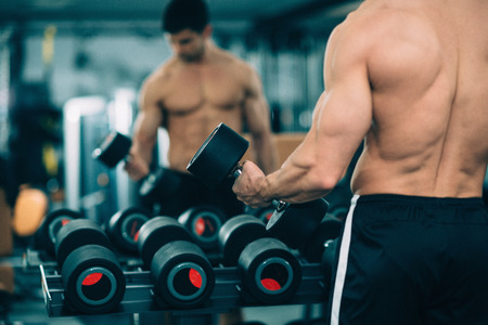 Muscular man exercising in the gym. Standing in front of mirror, picking weights from rack. Slightly toned imageの写真素材