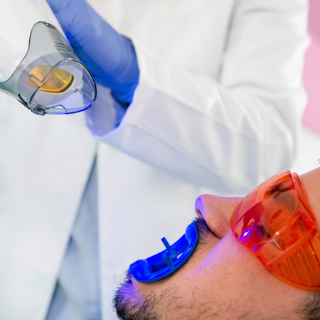 Dentist placing teeth whitening lamp over patient's mouthの写真素材