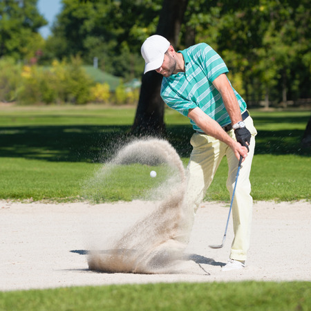 Golfer hits the ball out of sand trap. Focus on golfer, ball and sand wave in motion blur.の写真素材