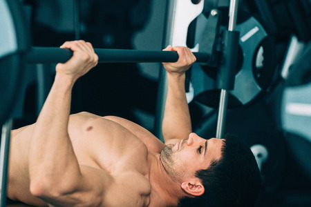 Muscular man lifting weights, lying on weight bench in gym. Toned imageの写真素材